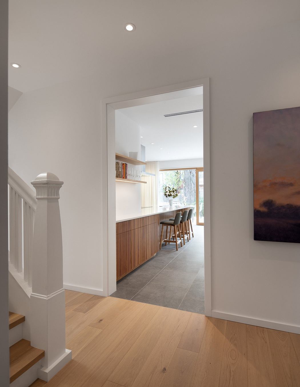 View from a hallway into a modern kitchen with wooden floors and a dining area.