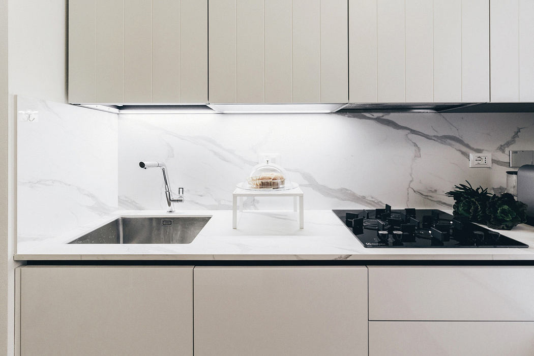 Modern kitchen with white marble backsplash and countertops, featuring a cake under a glass