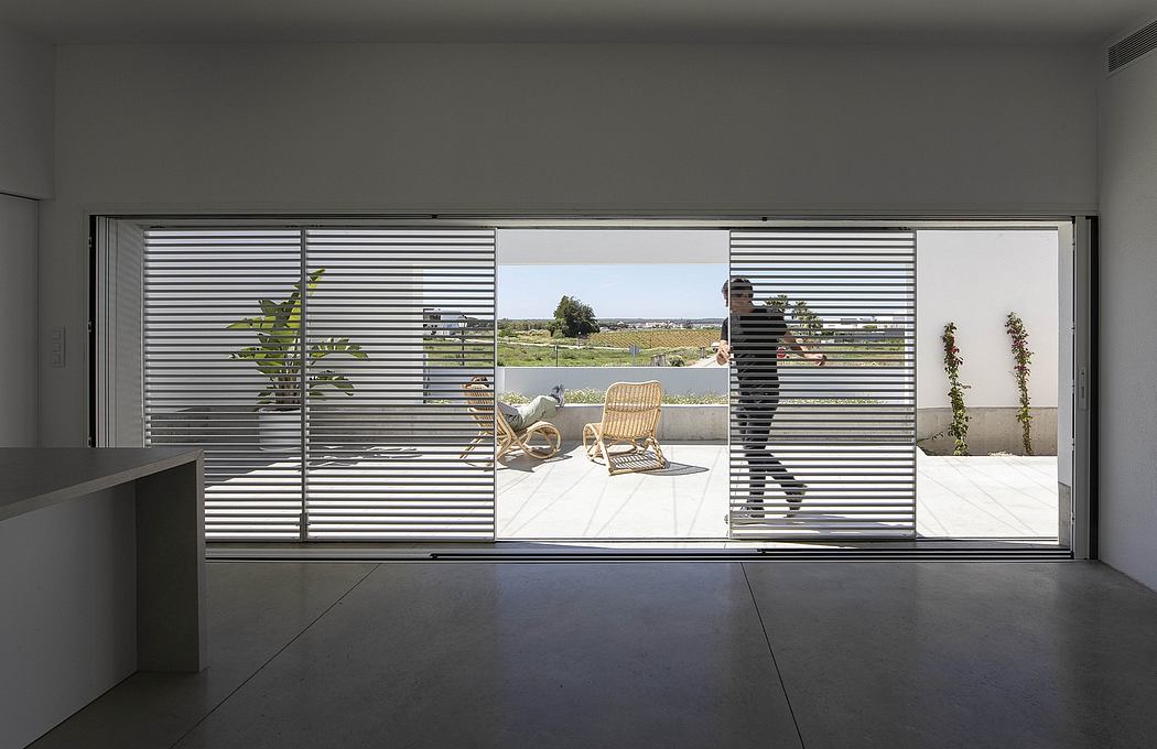 Modern room with large window overlooking a terrace with a person standing by the blinds.