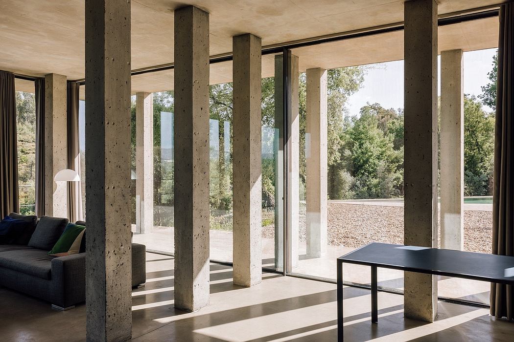 Modern interior with concrete pillars, large windows, and minimal furniture.