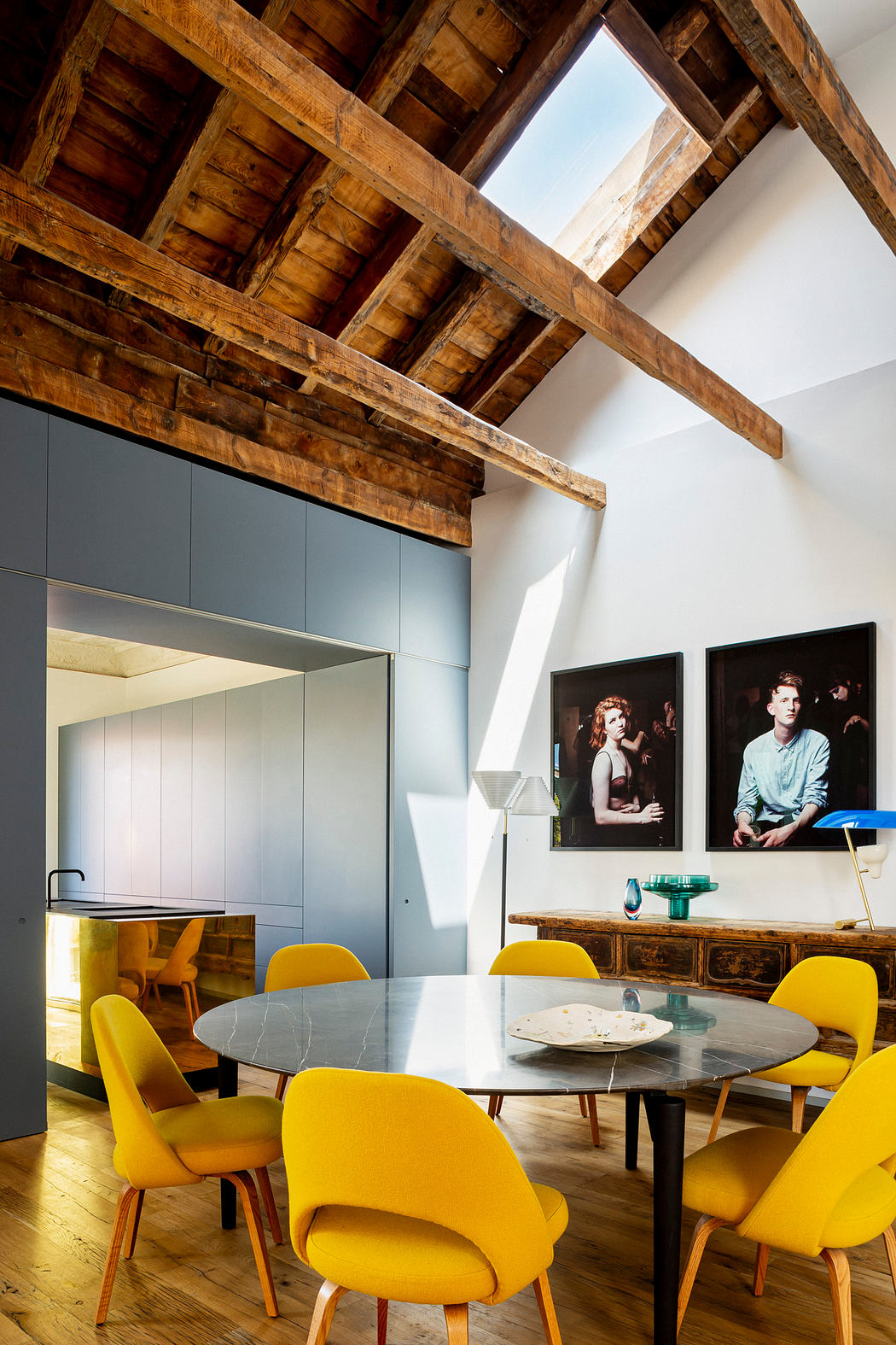 Modern kitchen with yellow chairs, a wooden ceiling, and artwork.