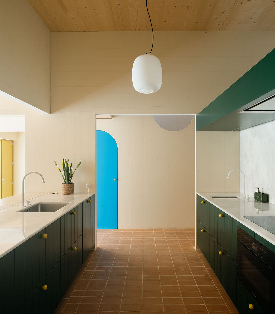 Modern kitchen with wooden ceiling, terracotta floor, and blue door.