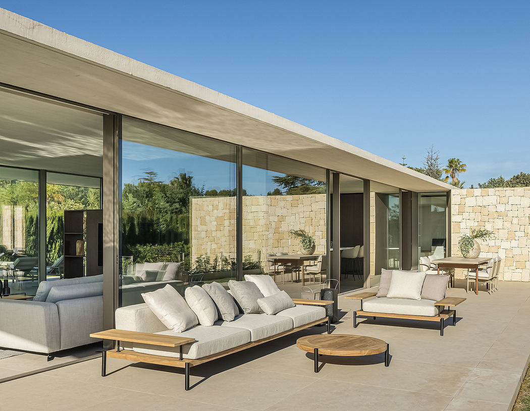 Modern patio with outdoor furniture, large glass windows, and stone walls under a clear