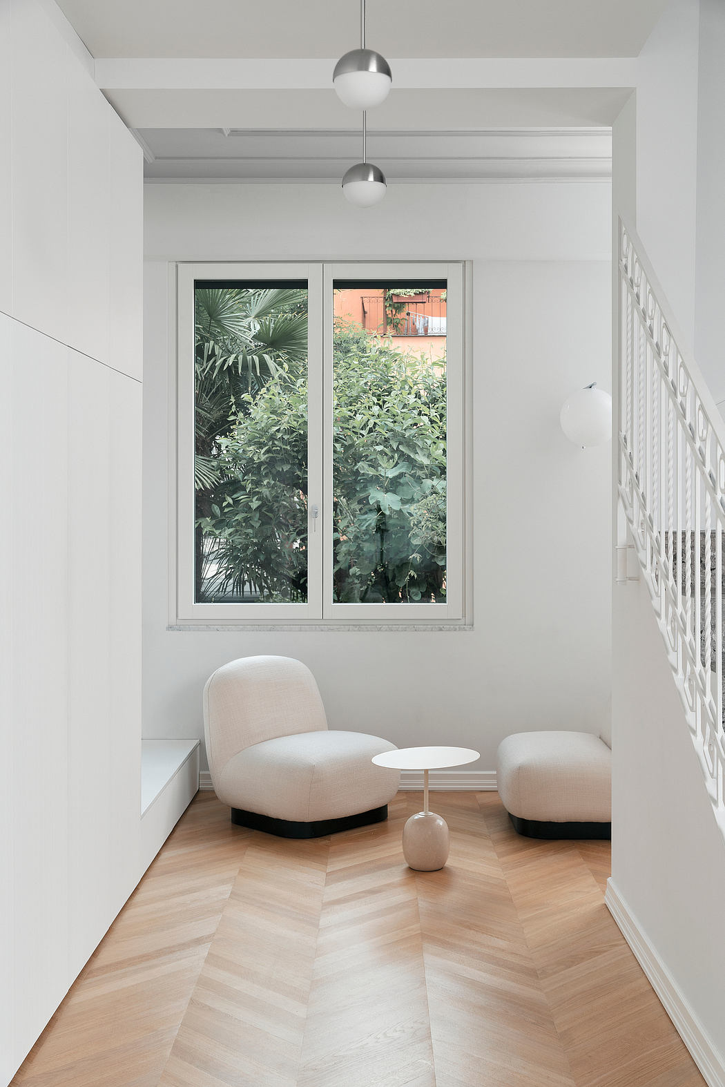 Modern white hallway with chairs, table, and a window view of greenery.