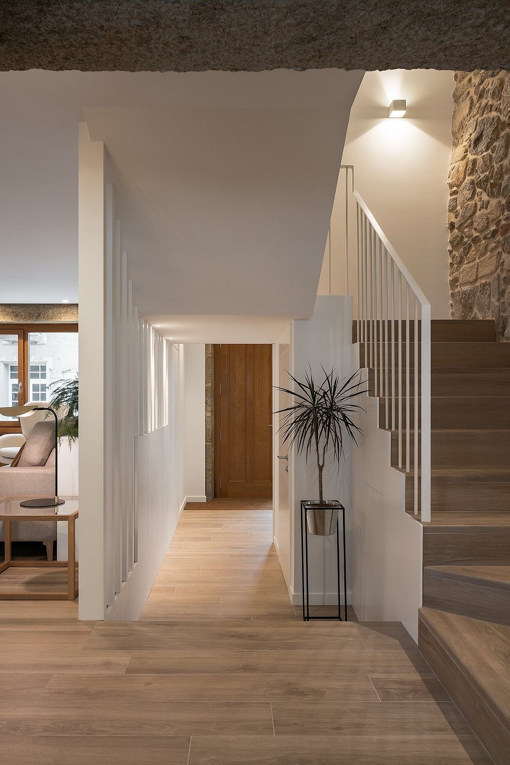 Modern interior with wooden stairs, white walls, and a stone accent wall.