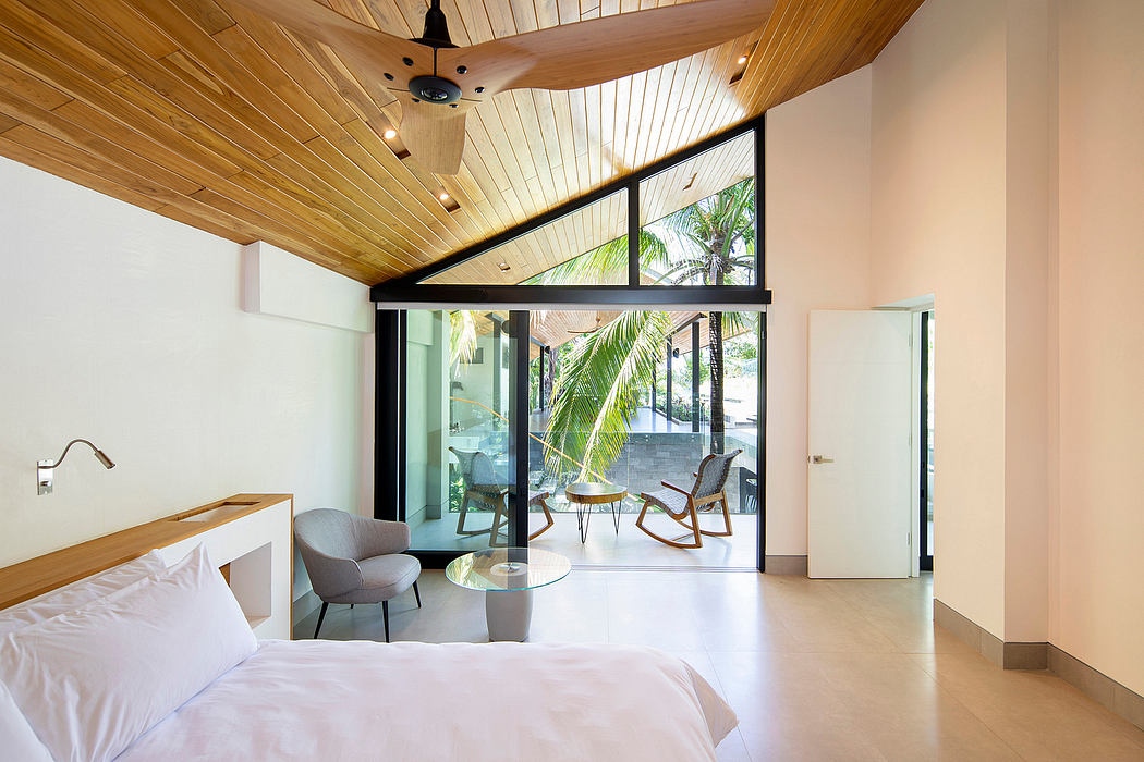 Modern bedroom interior with wooden ceiling, sliding glass door, and tropical view.