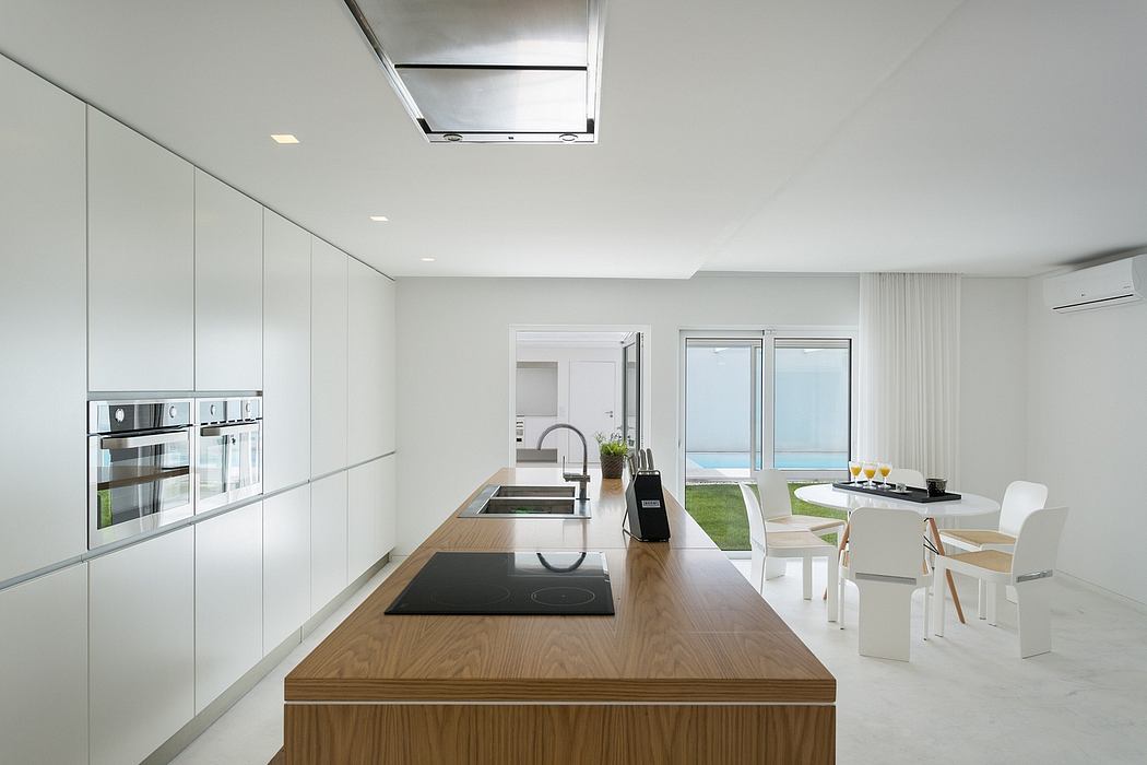 Modern kitchen with white cabinets, wooden island, and dining area overlooking the sea.
