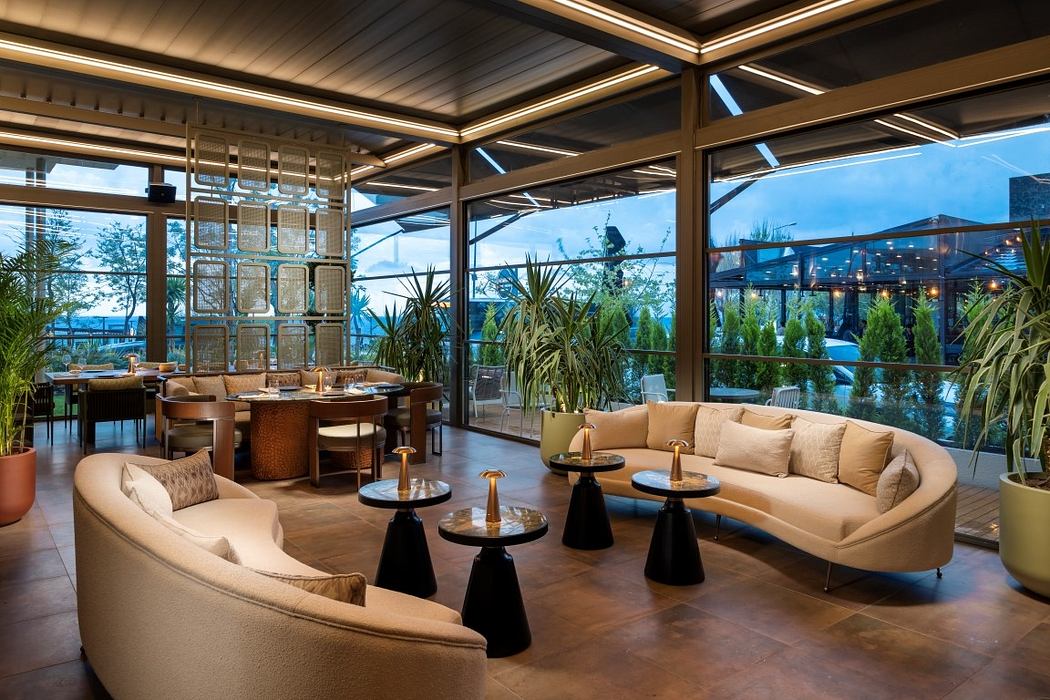 Modern lounge area with circular couches, wooden tables, and large windows.
