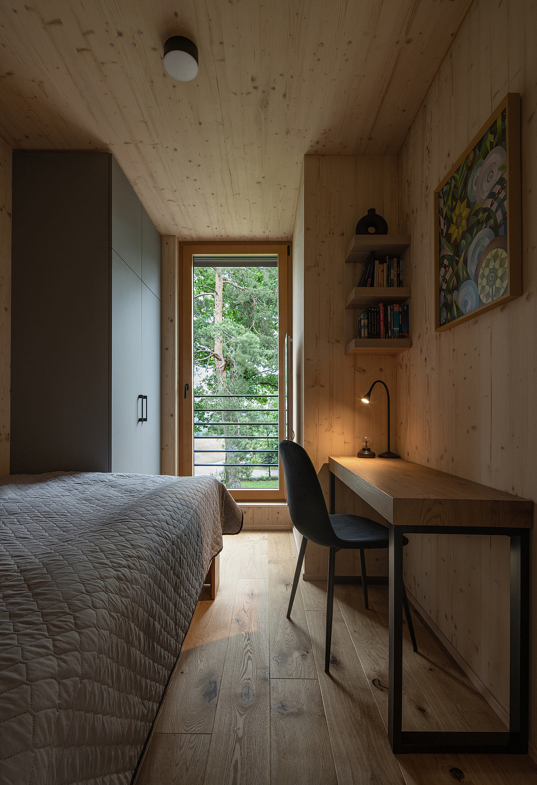 Cozy minimalist bedroom with wooden walls and a study area, overlooking trees.