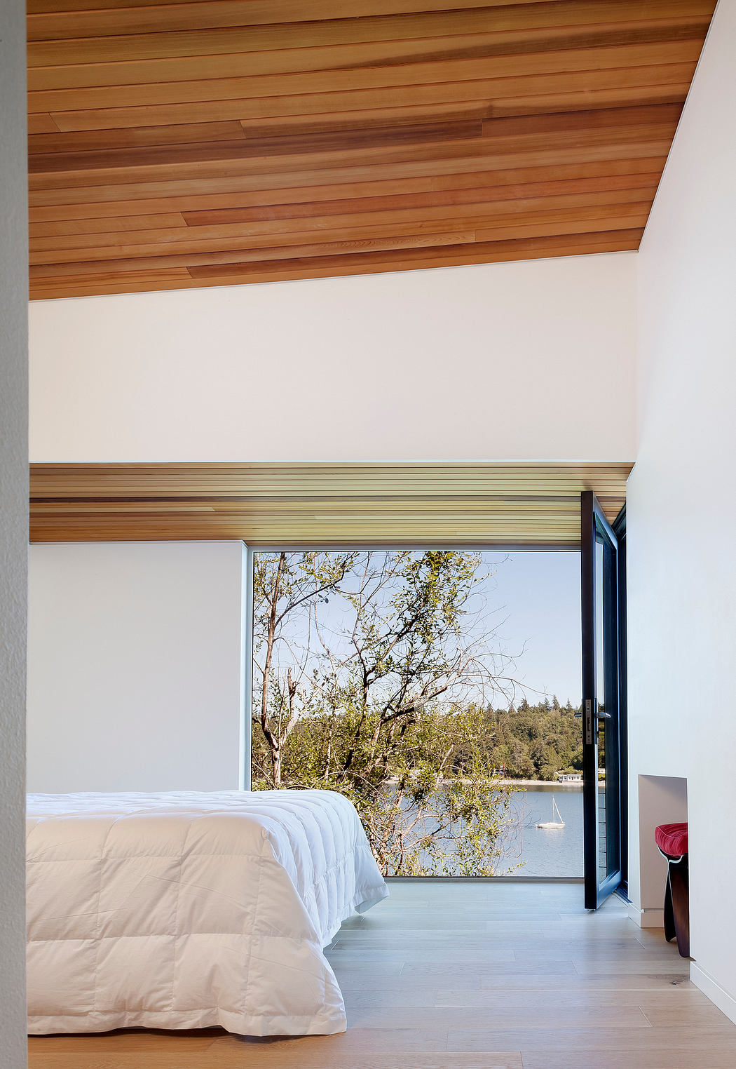 Bedroom interior with wooden ceiling and lake view through window.