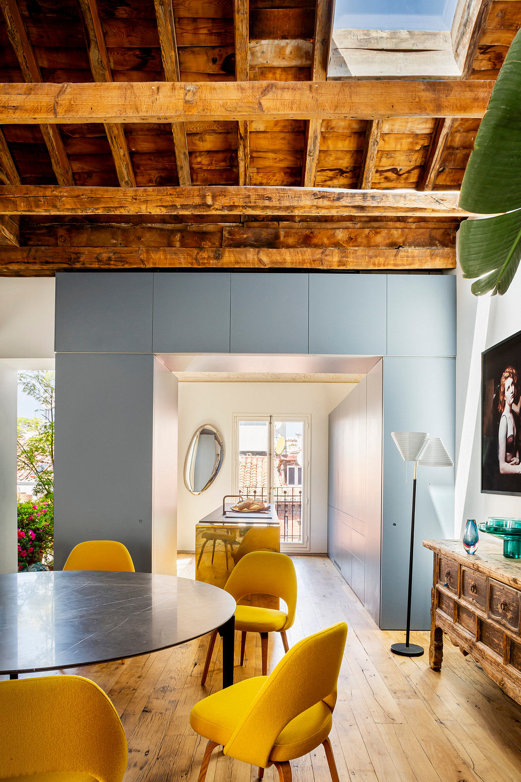 Modern dining room with yellow chairs, wooden ceiling beams, and rustic sideboard.