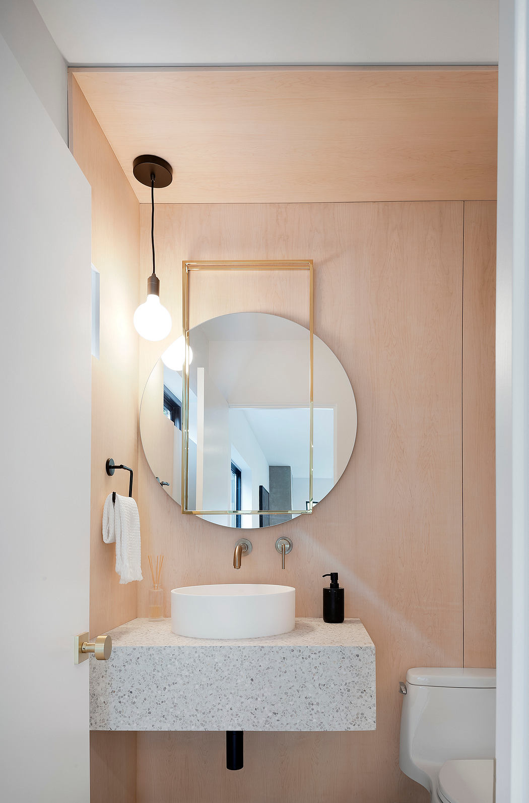 Minimalist bathroom with wood walls, round mirror, and white basin.