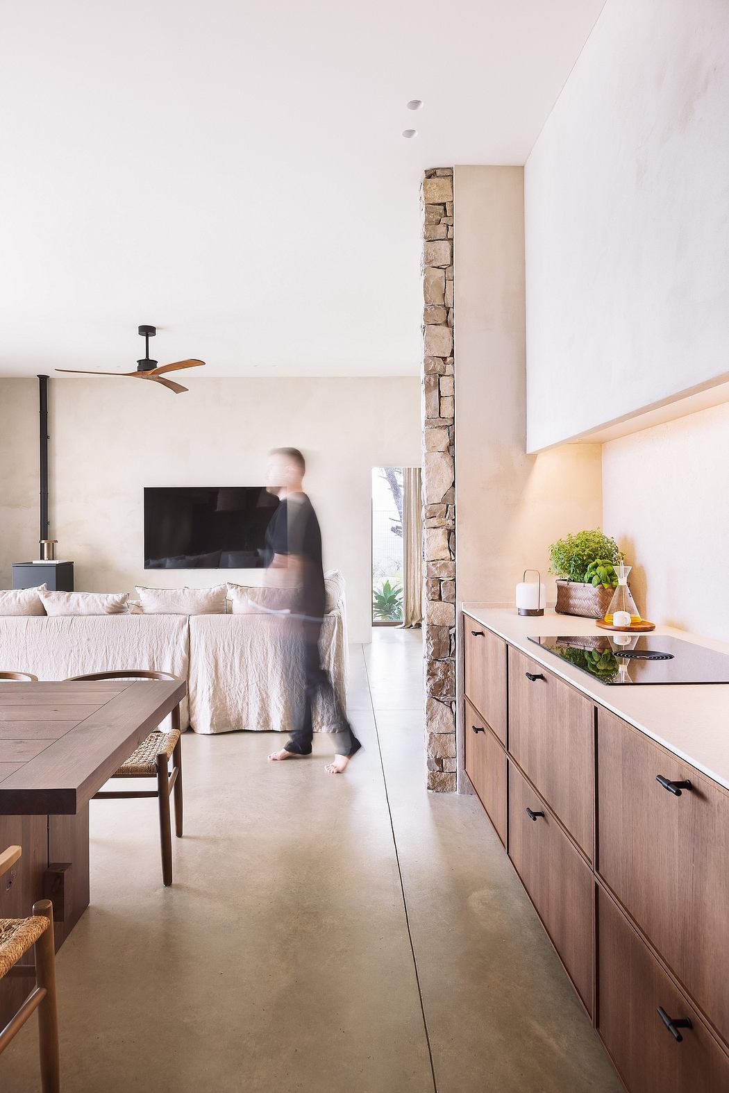 Modern interior with kitchen cabinets, stone column, and blurry person walking.