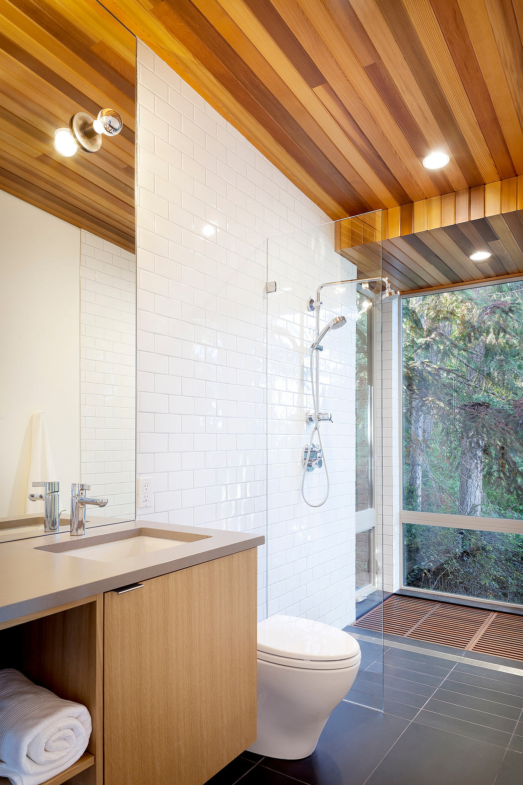 Modern bathroom with wooden ceiling, white tiles, and large window.