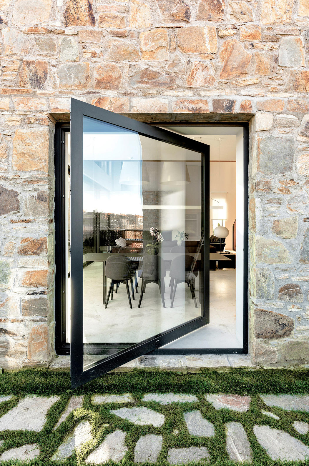 Modern pivoting glass door on a traditional stone wall facade.