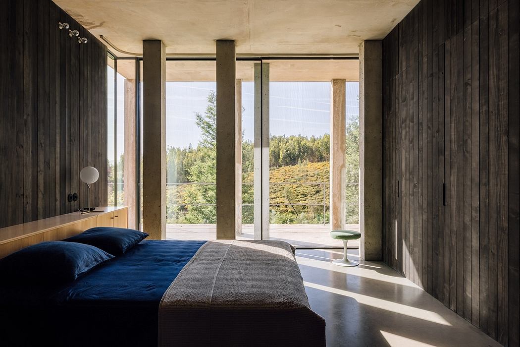 Modern bedroom with wooden walls, large windows, and forest view.