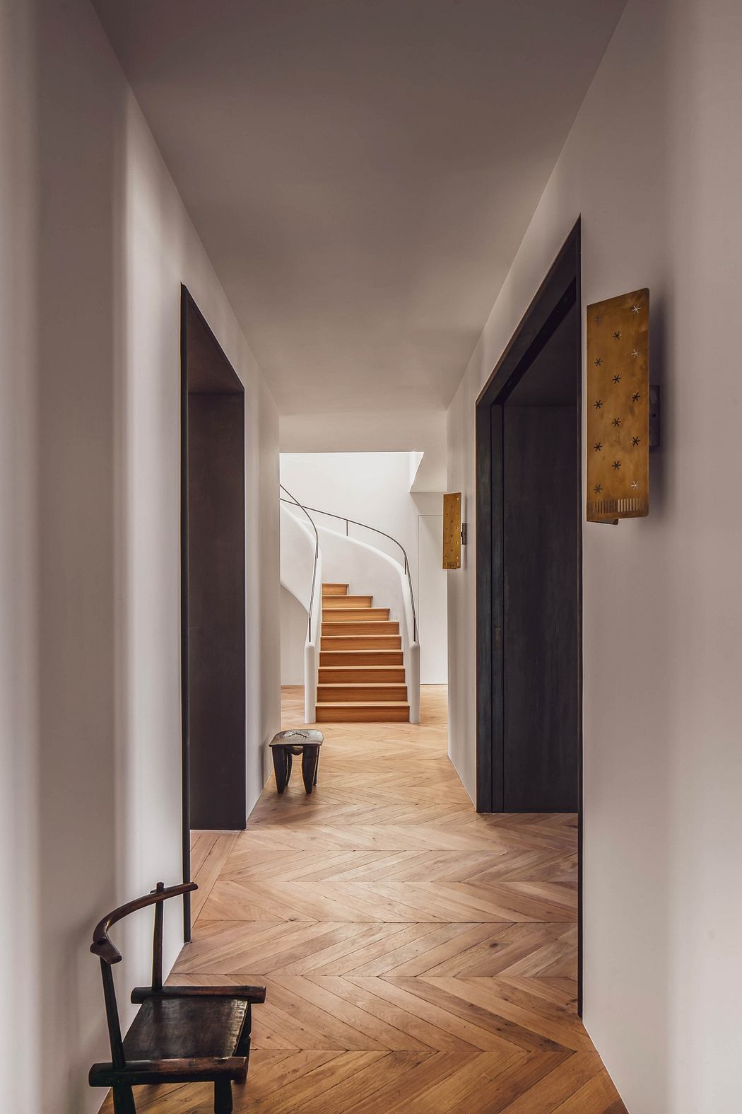 Elegant hallway with herringbone flooring leading to a curved staircase.