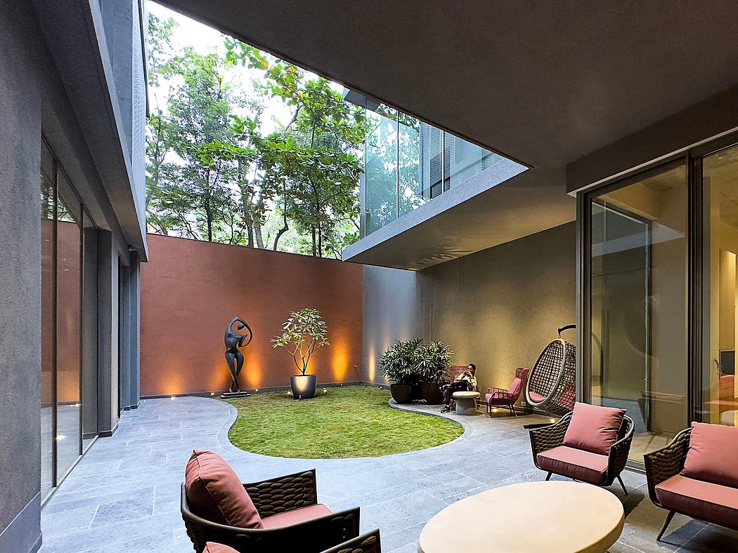 Modern courtyard with seating area, lawn, and sculpture, enclosed by building and glass