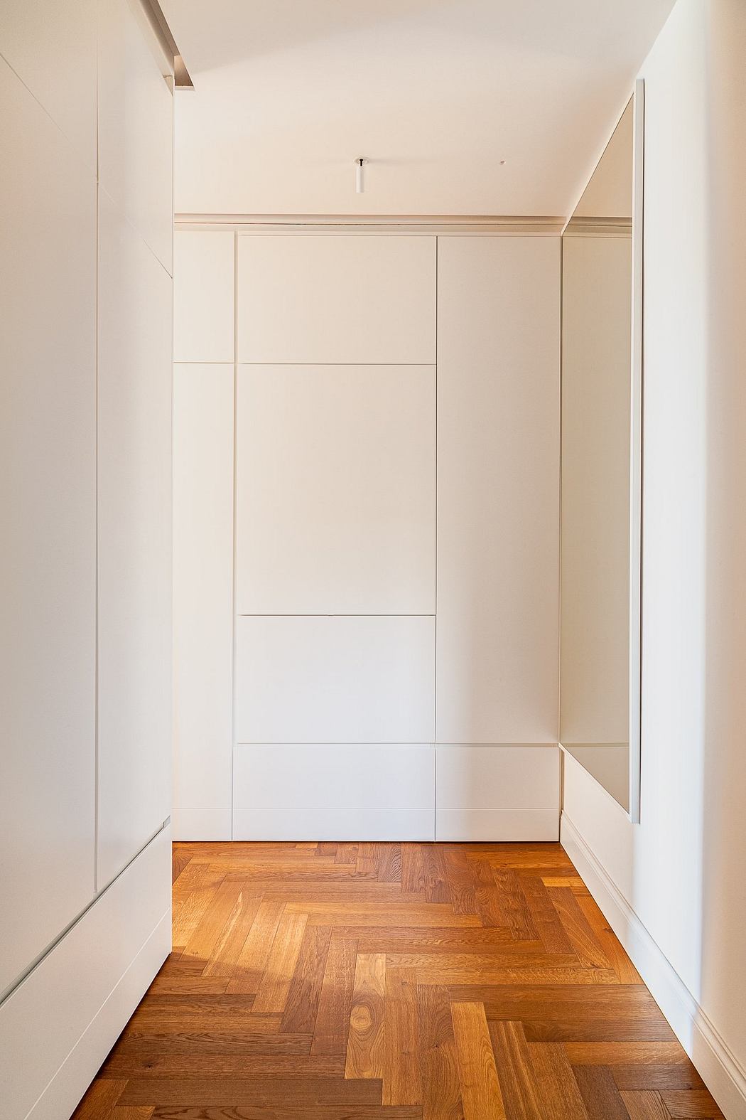 Minimalist interior with white walls and herringbone wood flooring.