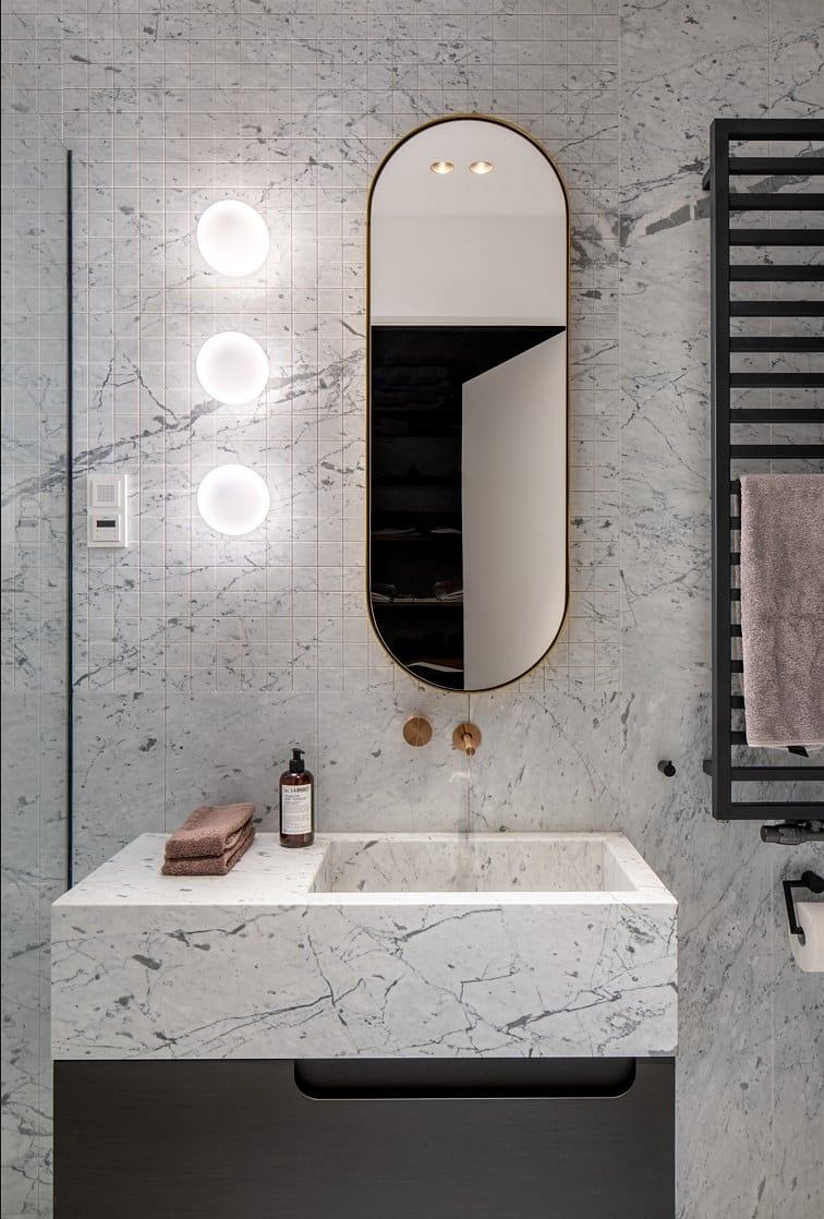 Chic bathroom with marble walls, oval mirror, and globe lights.