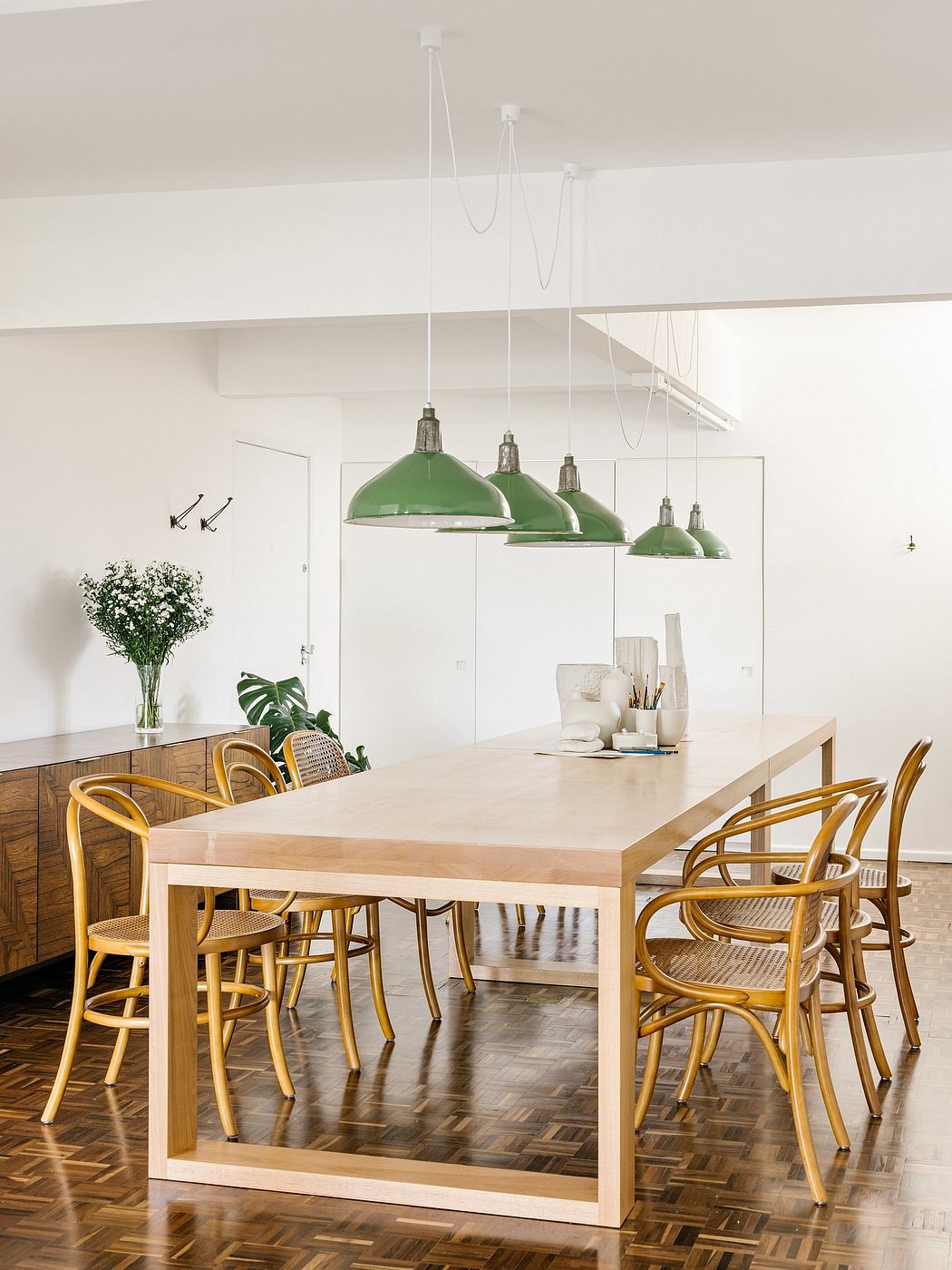 Modern dining room with a wooden table, rattan chairs, and green pendant lights
