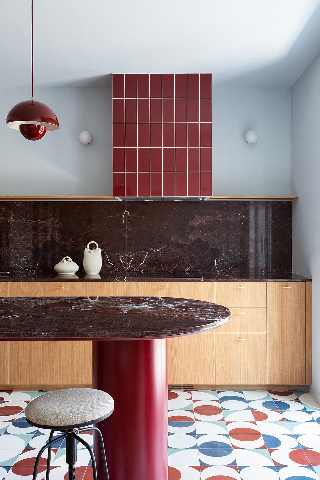 Modern kitchen corner with geometric-patterned floor, marble-top table, and red accents