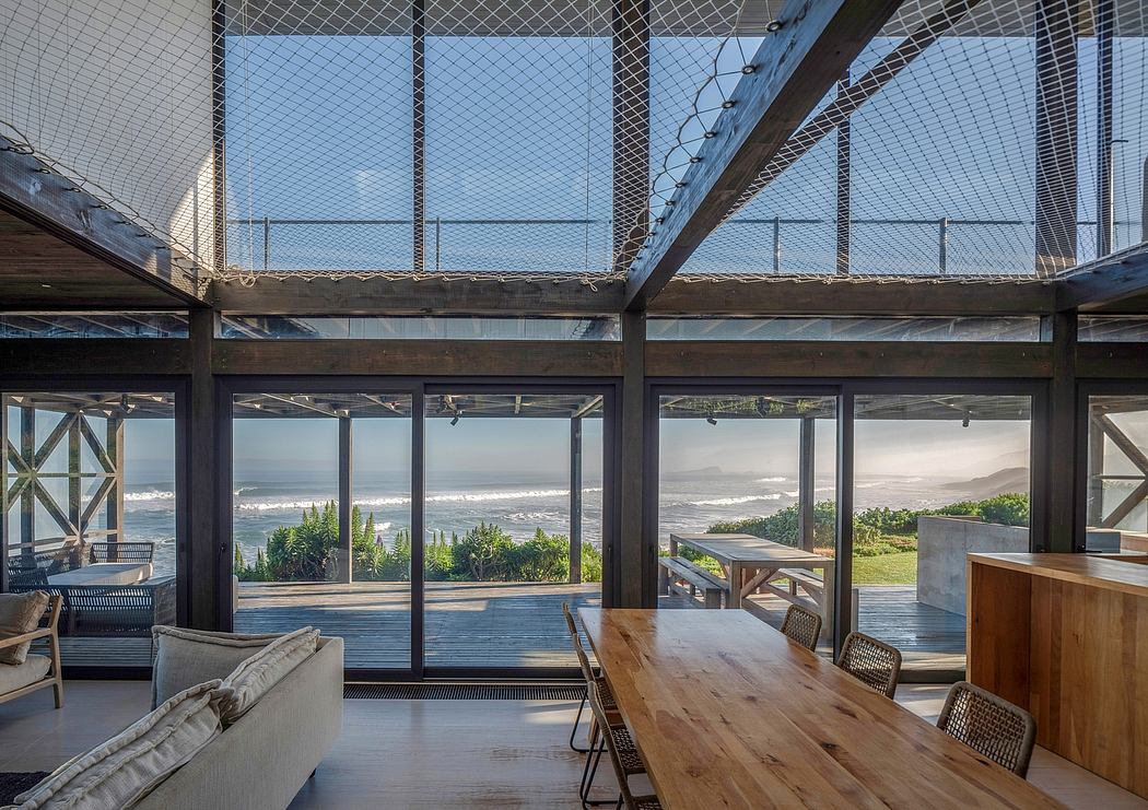 Modern room with large windows overlooking the sea, featuring a wooden table and mesh loft