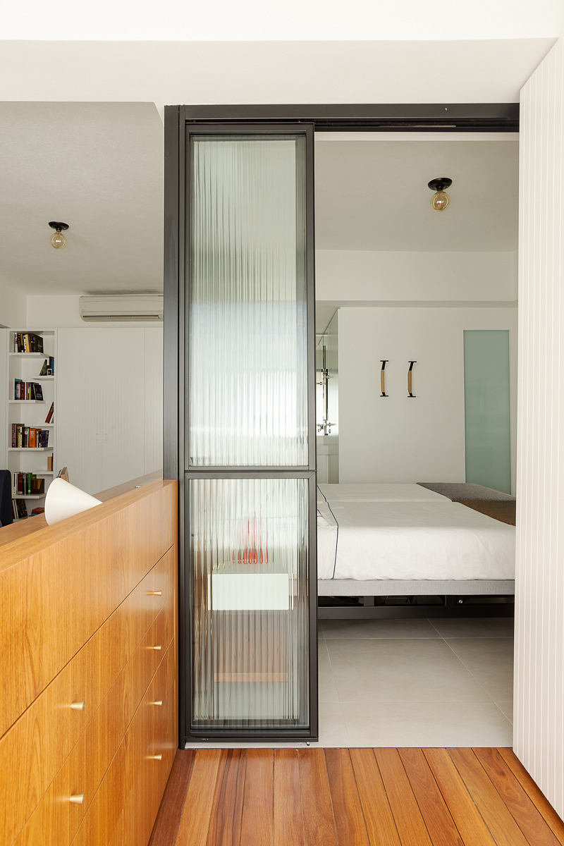 Sleek bedroom with sliding frosted glass door and wood flooring.