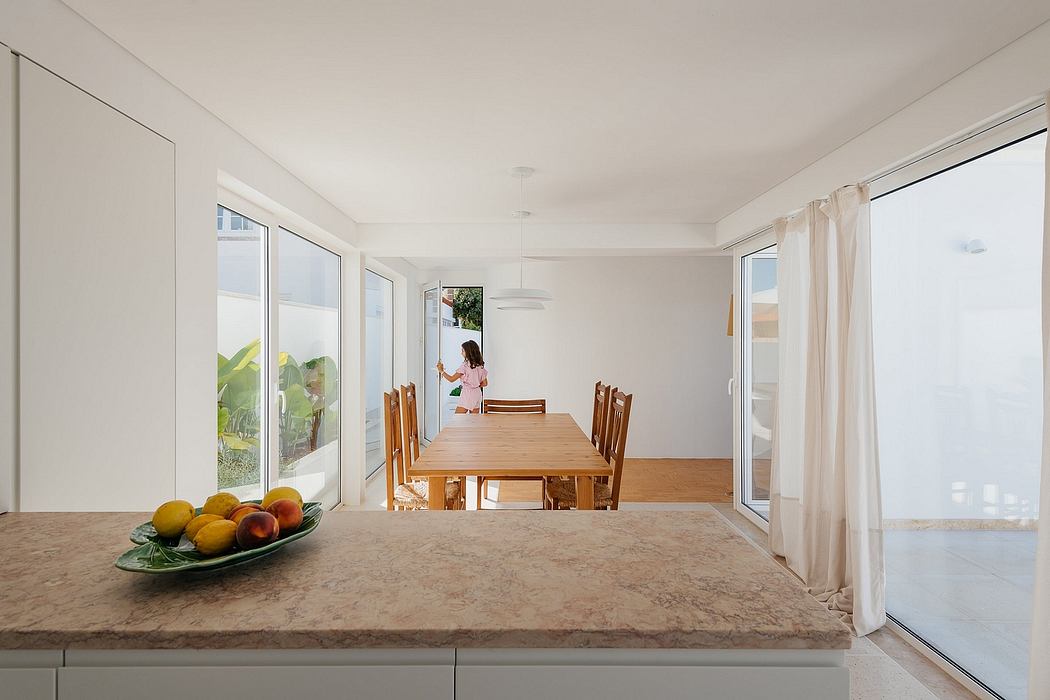 Bright dining room with wooden table, chairs, and fruit bowl on countertop.