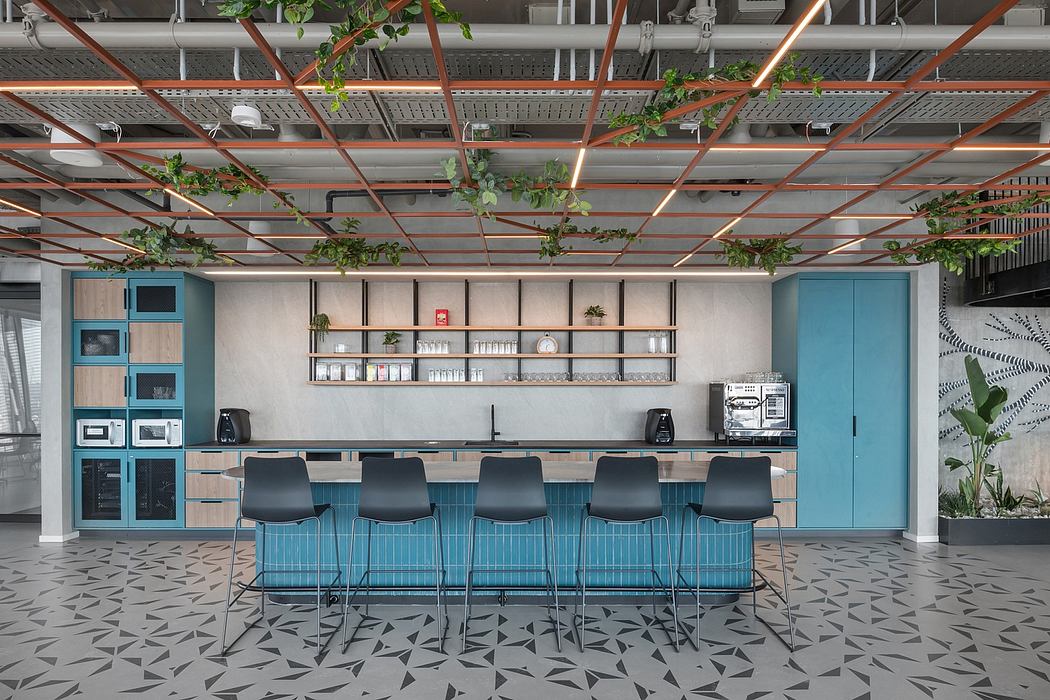 Modern office kitchen area with blue chairs and exposed ceiling.