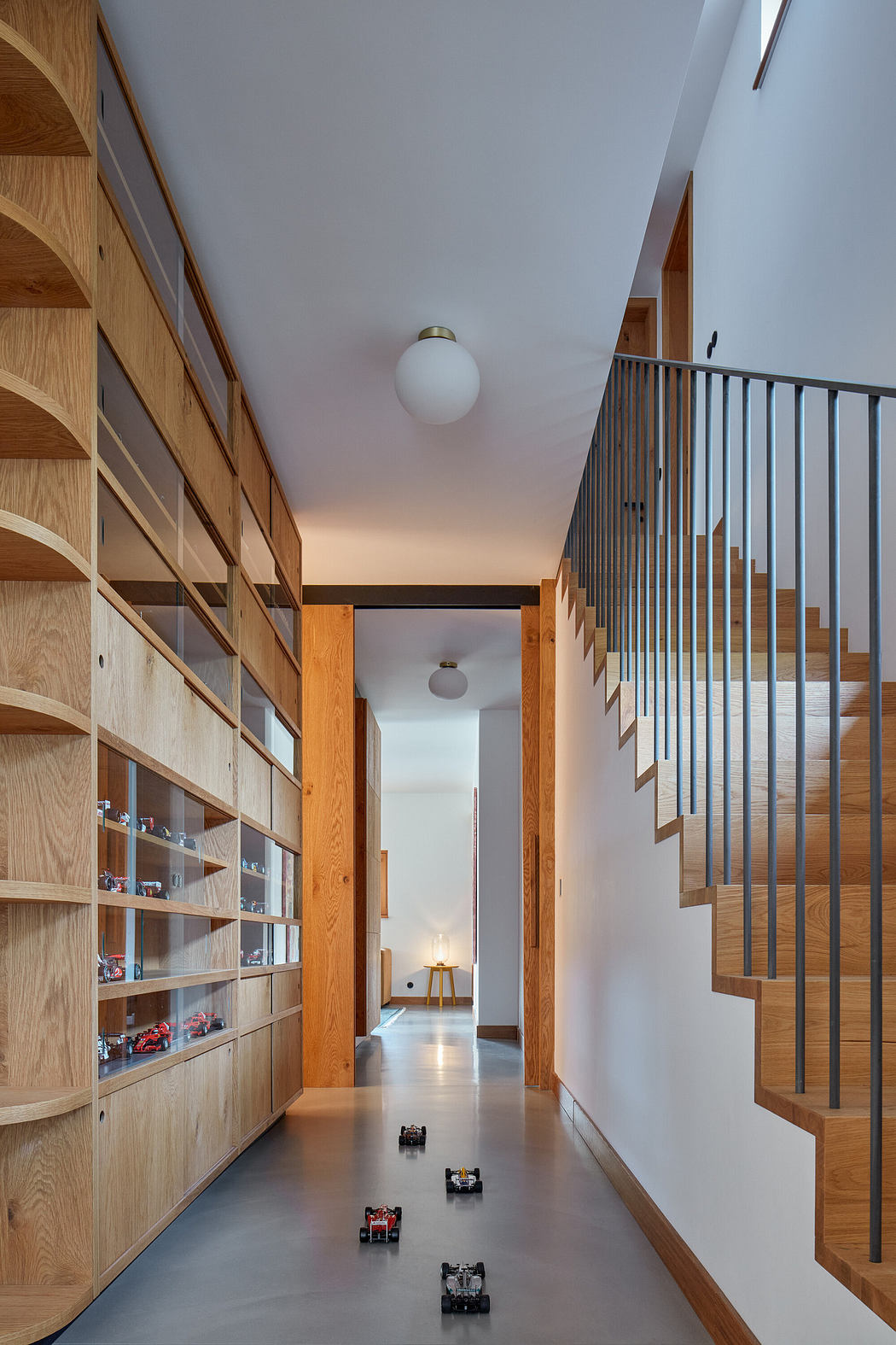 Modern hallway with wooden shelves, staircase railing, and toy cars on the floor.
