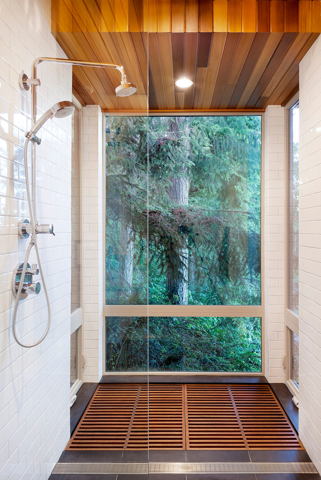 Modern shower with wooden ceiling and large window overlooking trees.