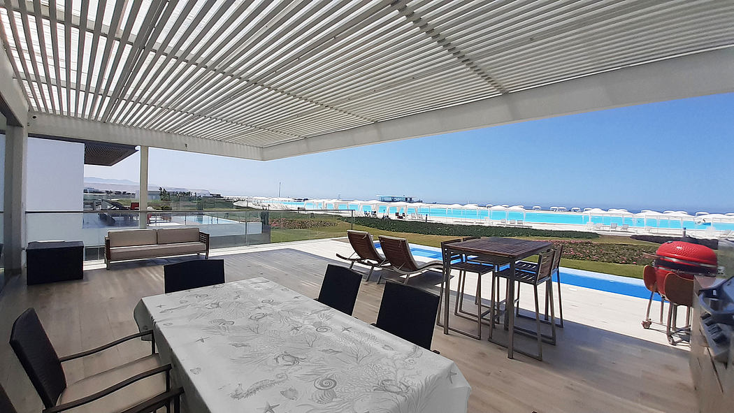 Sleek patio with slatted roof, dining set, and ocean view.