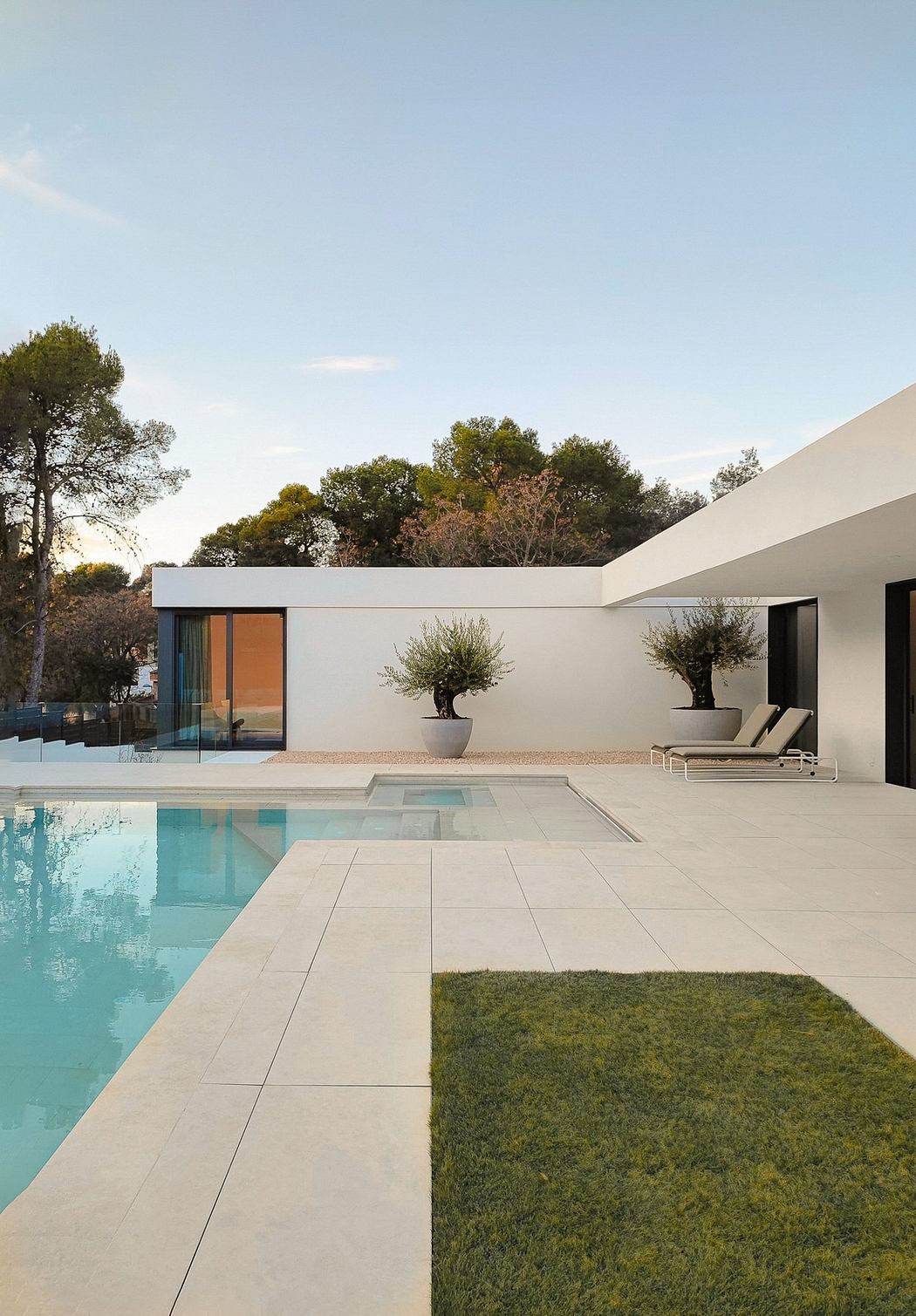 Minimalist poolside with sleek white villa, large windows, and manicured green