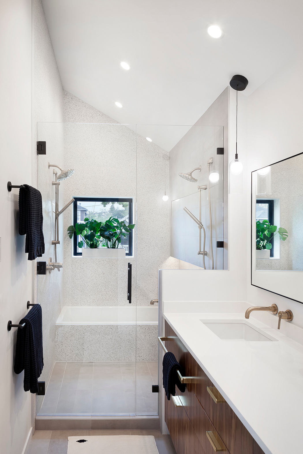 Modern bathroom with a tub, white walls, wooden vanity, and greenery outside