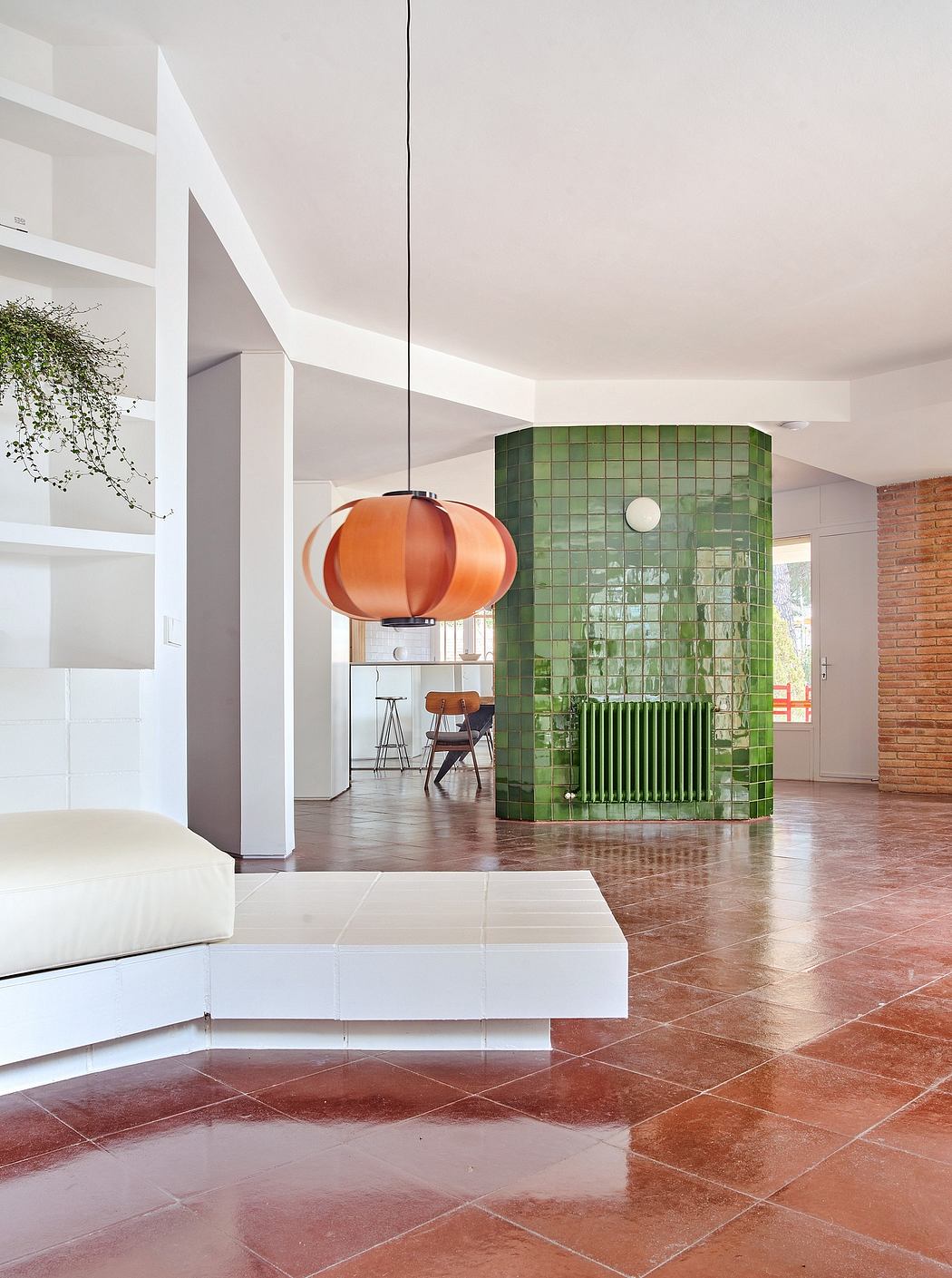 Modern room with orange pendant light, green tiled column, and minimalistic furniture.