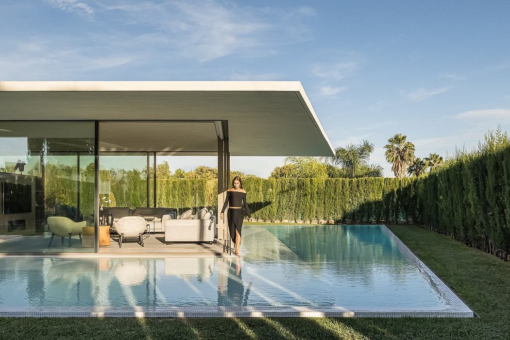 Sleek glass-walled house overlooking a pool with verdant hedges and