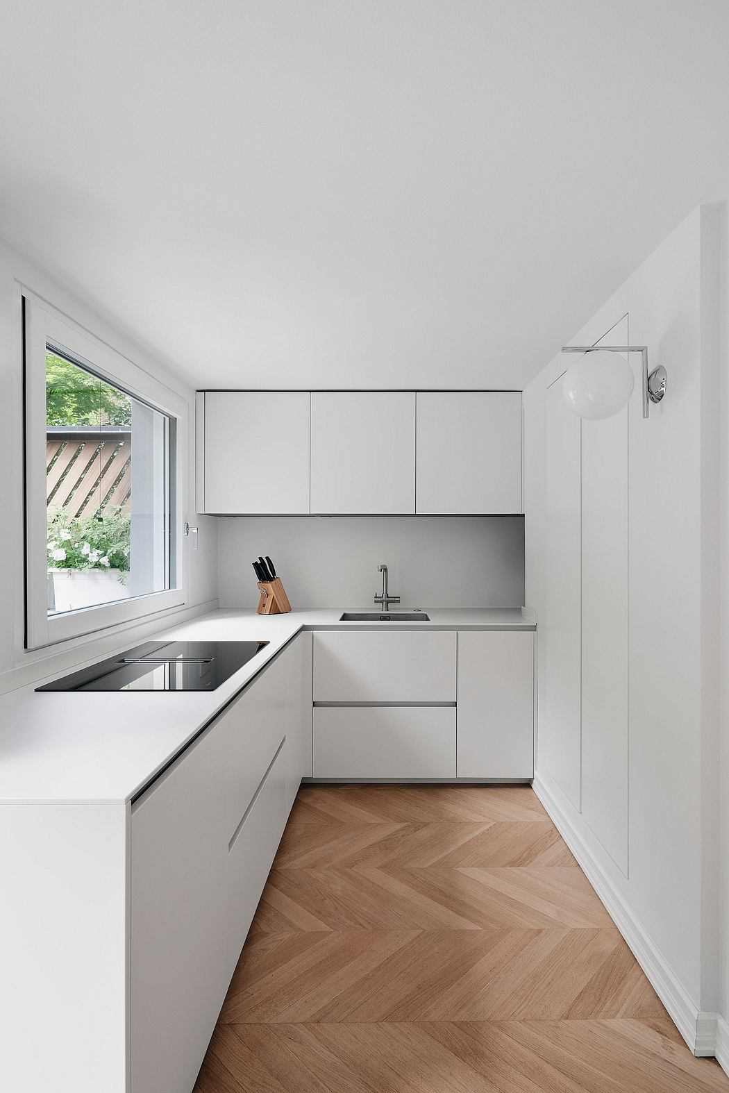 Modern, minimalist white kitchen with herringbone wood flooring.