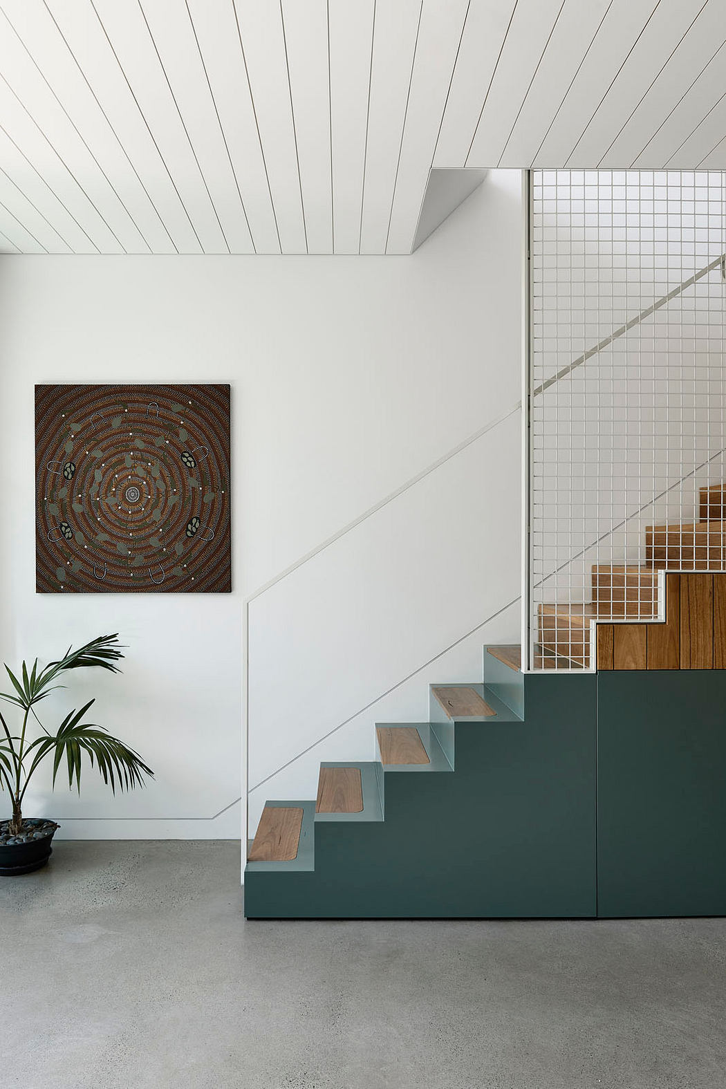 Modern staircase with white walls, green base, wooden steps, and artwork on the