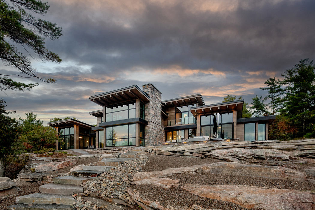 Contemporary glass-fronted house with stone pathways amidst natural landscape.