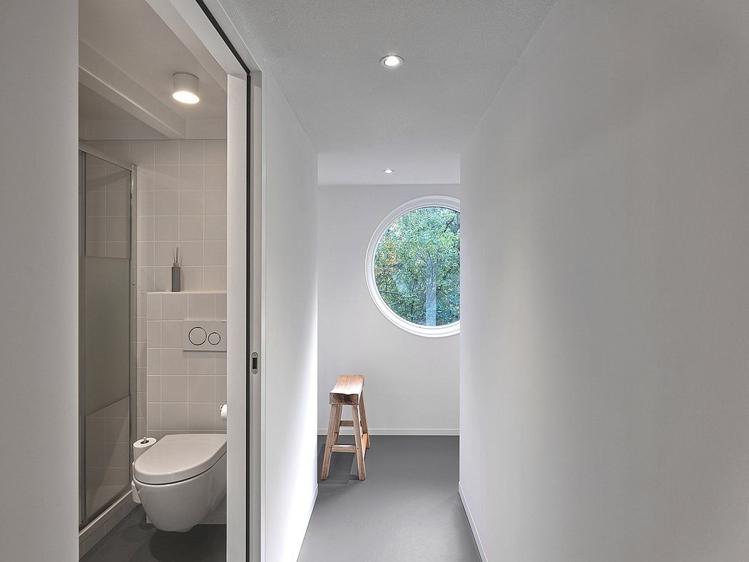 Modern bathroom with white walls, round window, and wooden stool.