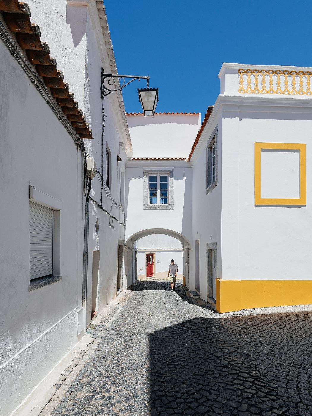Narrow cobbled street with white traditional buildings and a person in the distance.