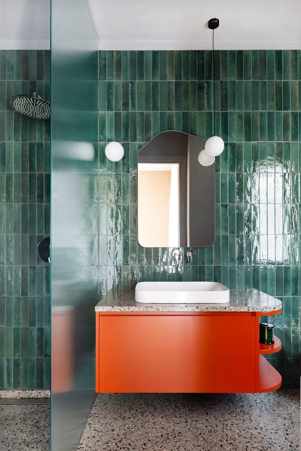 Modern bathroom with green tiles, orange vanity, and arch mirror.