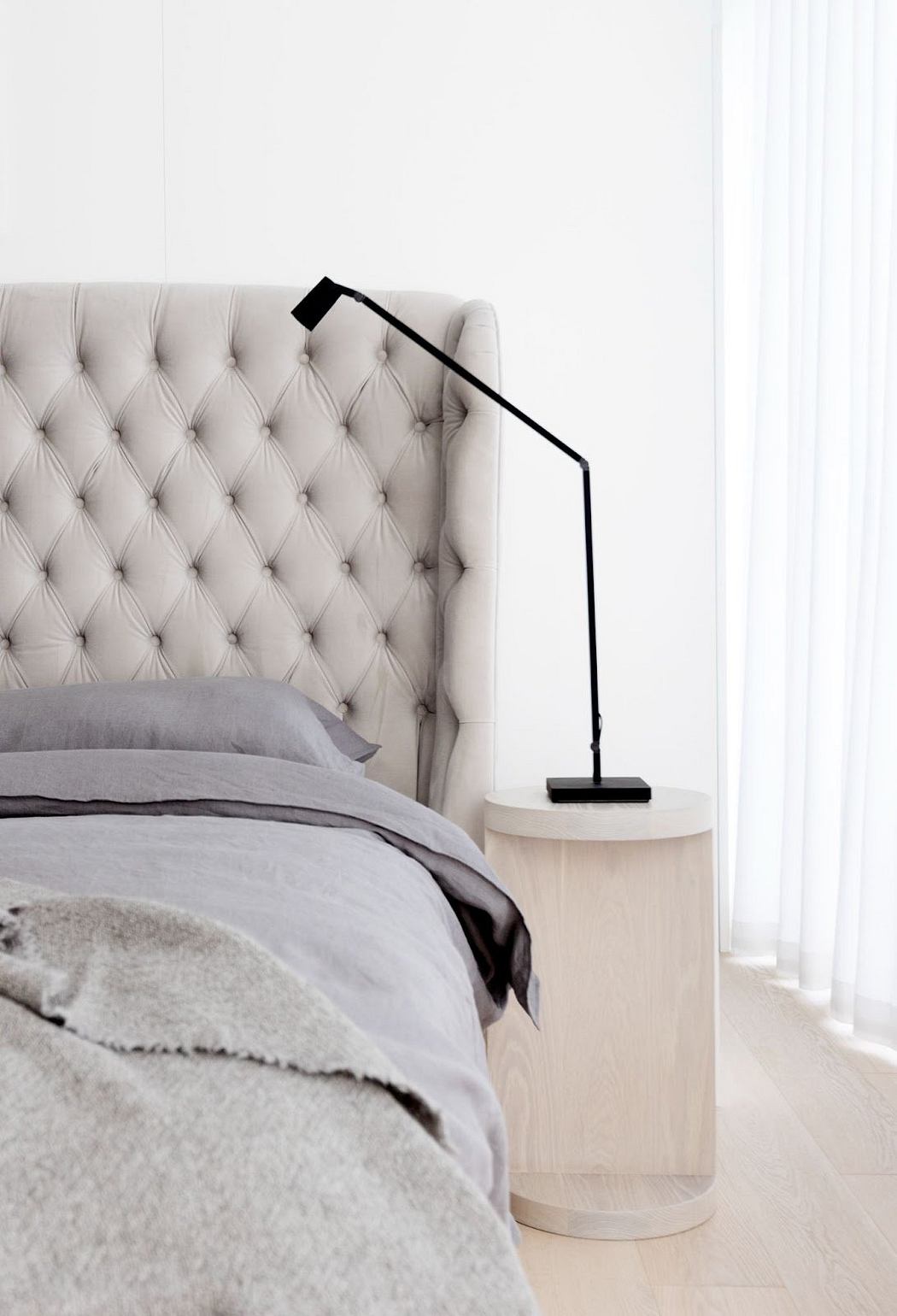 Minimalist bedroom with tufted headboard and modern bedside lamp.