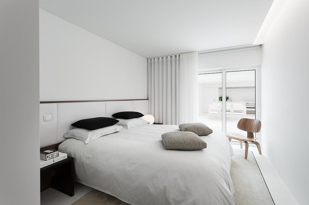 Minimalist white bedroom with large window and simple furnishings.
