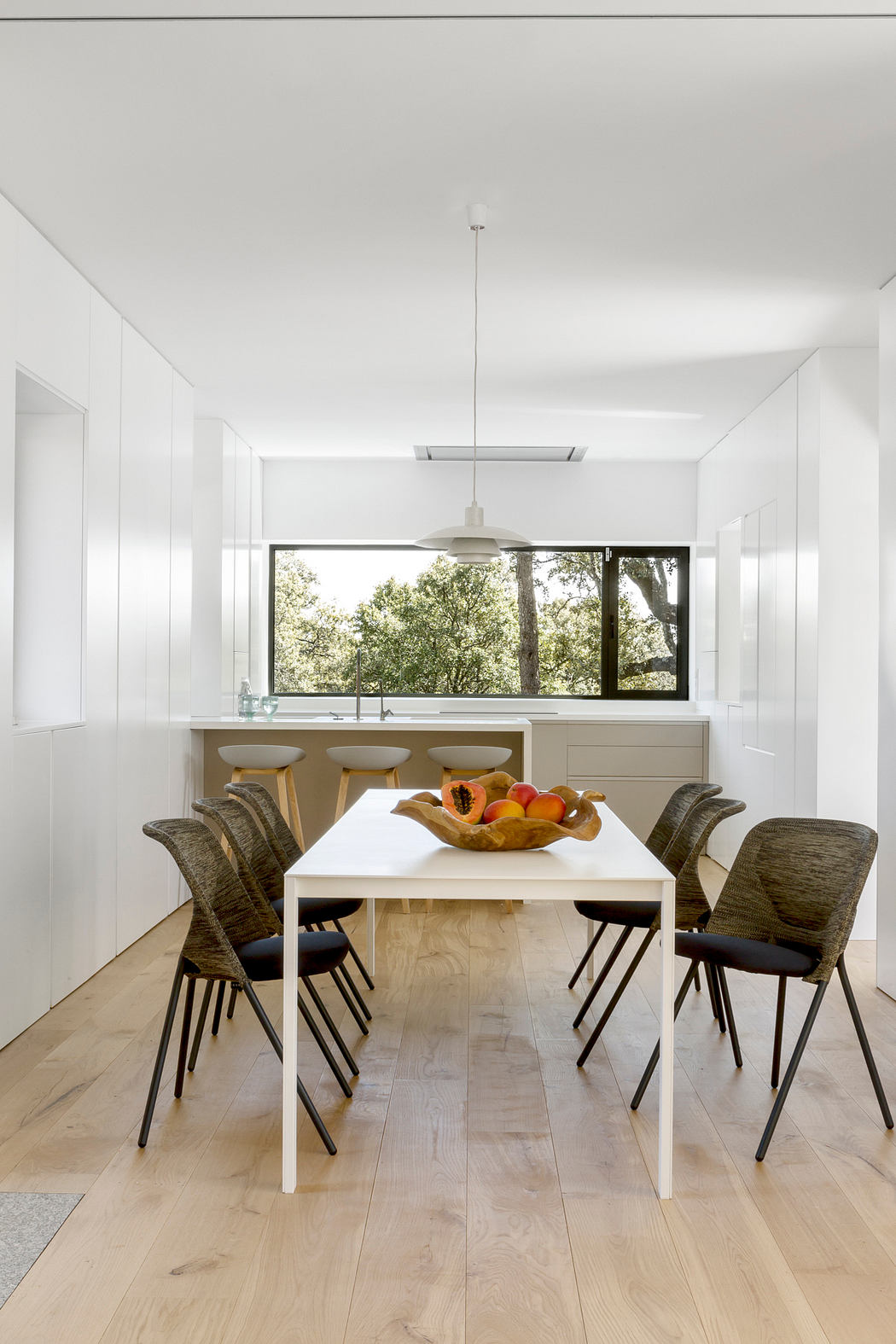 Modern dining room with white walls, a wooden floor, and a large window.