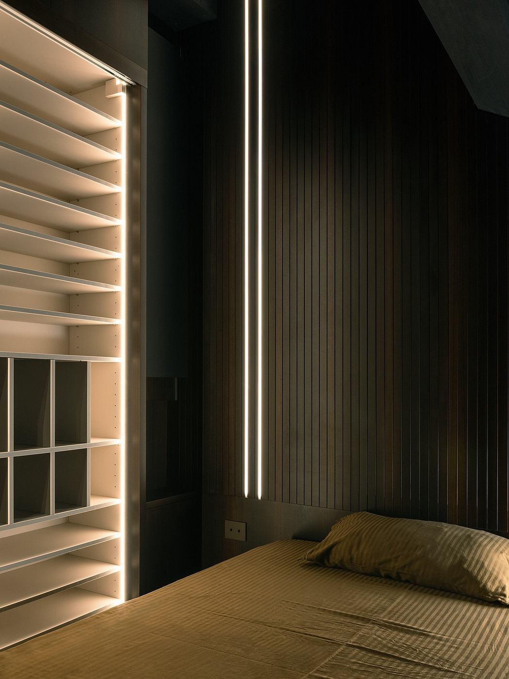 Modern bedroom with vertical lighting and dark tones.
