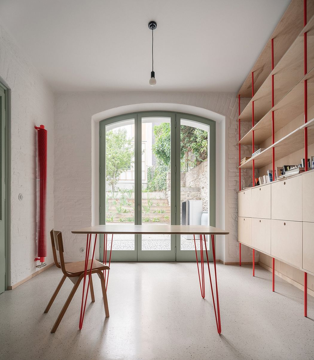 Minimalist room with red-accented furniture and arched window.