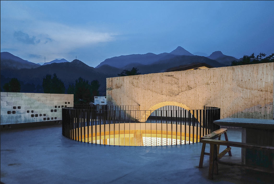 Modern outdoor terrace with a circular pool lit at dusk, mountains in the background.
