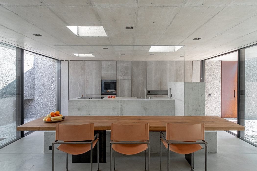 Minimalist kitchen with a wooden table, tan chairs, and concrete walls.